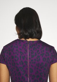 Lila klänning med ett svart leopardtryck. Har korta ärmar och en dragkedja i ryggen för enkel påklädning. Slät tygtextur.