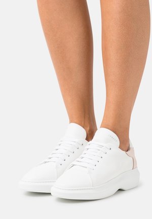 White leather sneakers with a smooth texture, rounded toe, laces, and a pink accent near the heel. Minimalist design, clean lines.