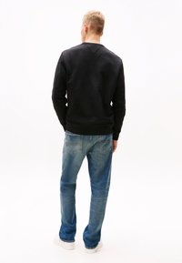 Black sweatshirt with ribbed cuffs and hem, paired with medium blue denim jeans. The outfit features a relaxed fit and minimal detailing.