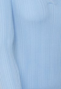 Pull bleu clair à côtes avec un col en V, des manches longues et une texture douce. Présente des lignes verticales et un design ajusté.