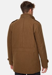 Manteau en mélange de laine marron avec un col montant, des épaulettes et une coupe droite. Il présente une couture dorsale et des sangles de poignet ajustables.