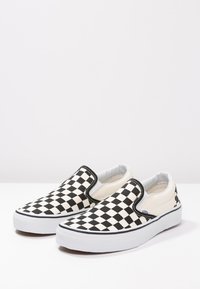 Svart og hvit rutete slip-on lerretsko med elastiske sidetilbehør og hvit gummisåle. Glatt tekstur og rund form.