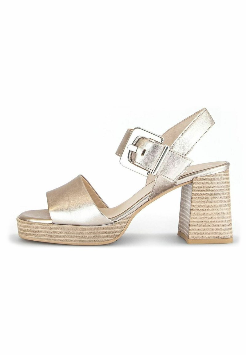 Sandale femme dorée métallisée à bout ouvert avec talon épais empilé et large bride à boucle à la cheville sur fond blanc.