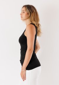 Top smanicato nero realizzato in tessuto elasticizzato, con una silhouette aderente e scollo rotondo, abbinato a pantaloni bianchi.