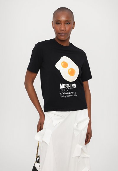 Tricou negru din bumbac cu un grafic reprezentând două ouă prăjite și litere albe. Asortat cu o fustă albă cu detalii de dantelă.
