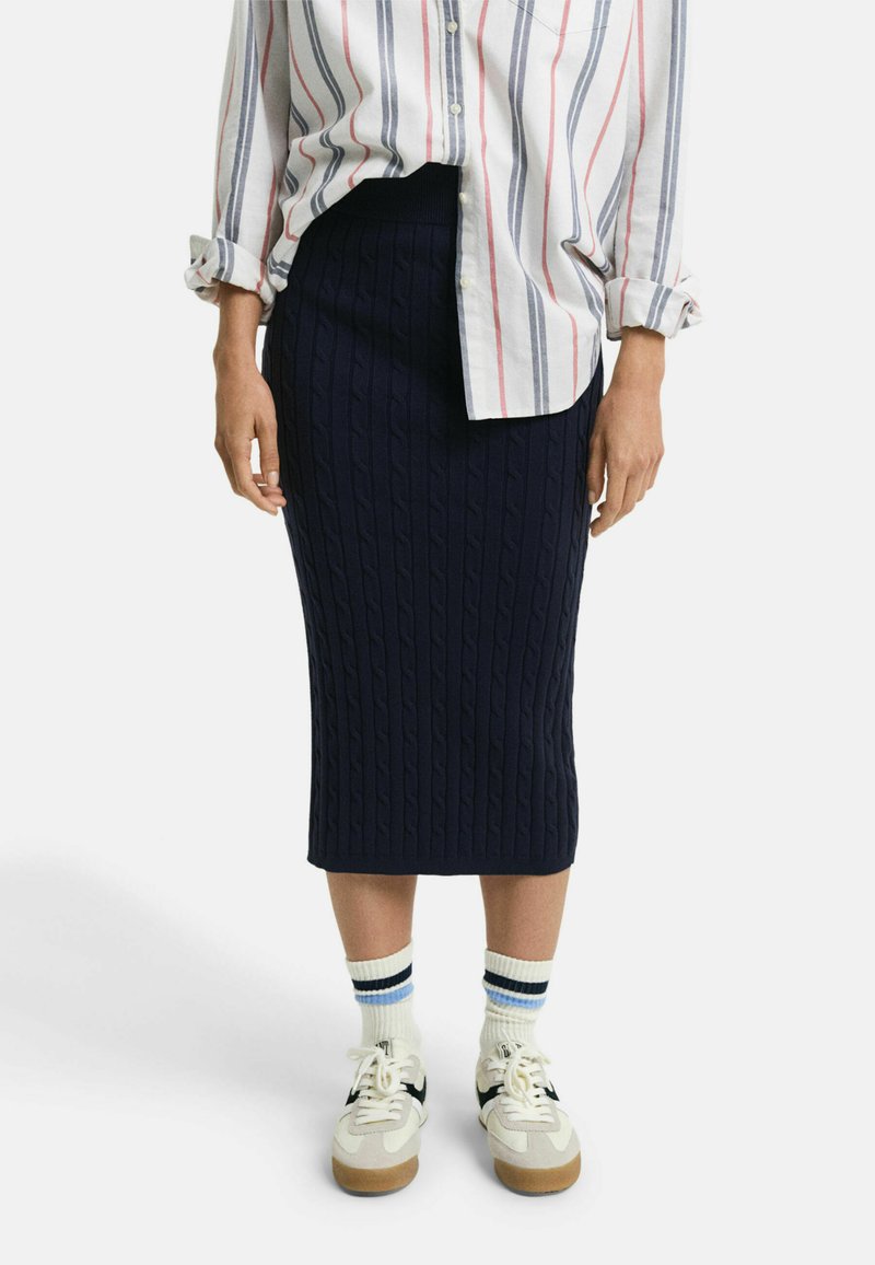 Gonna midi in maglia blu navy, con vita a costine, abbinato a una camicia bianca e scarpe sportive. Calzini bianchi con strisce blu e nere.
