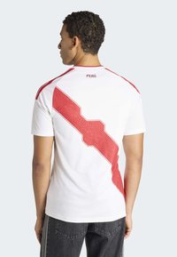 Wit atletisch shirt met een gedurfd rood diagonaal patroon en "PERÚ" tekst boven de kraag; heeft rode accenten op de schouders.