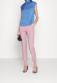 Niebieski satynowy top bez rękawów z wysokim dekoltem, zestawiony z dopasowanymi różowymi spodniami. Czarny, sandałowy obcas i mała czarna torebka dopełniają całość.