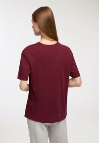 T-shirt corto maroon con colletto rotondo, vestibilità comoda e tessuto liscio, visto da dietro.
