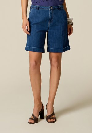 Vrouw die blauwe denim shorts met omslag draagt, gecombineerd met donkerbruine sandalen met hoge hakken en armbanden aan één pols.