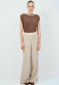 Bruine kortmouwtop met decoratieve kralen bij de halslijn, gecombineerd met hooggetailleerde, wijde beige broeken. Glad stoffen texturen.