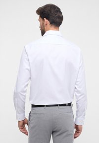Witte blouse met lange mouwen, een puntige kraag en knoopmanchetten, gecombineerd met lichtgrijze op maat gemaakte broek. Glad materiaal met een verzorgde uitstraling.