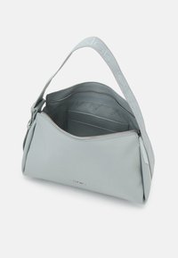 Sac d'épaule Calvin Klein gris clair avec une large bandoulière marquée, dézippé montrant les poches intérieures et la doublure avec logo.