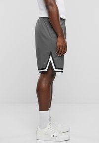 Grå idrottsshorts med vit och svart diagonal randdetalj vid fållen. Bärs med vita sneakers och synliga vita strumpor.