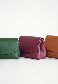 Tři tašky v zelené, burgundské a hnědé kůži. Každá má klopu, čisté linie a vyražené logo na přední straně.