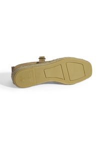 Schuhe mit einer flachen, strukturierten Gummisohle und einem hellbraunen Wildleder-Obermaterial, ausgestattet mit einem dekorativen Riemen und genähten Details.