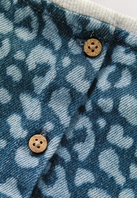 Denim fabric with a blue and light blue leopard print pattern, featuring wooden buttons at the top and a gray ribbed neck trim.