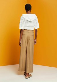 White knitted hoodie with a hood and short sleeves, paired with beige wide-leg trousers featuring a high waist and back pockets.