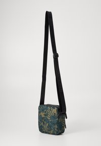 Borsa a tracolla quadrata con motivo floreale in turchese e verde. Cinturino nero regolabile e chiusura con zip. Tessuto morbido, design compatto.