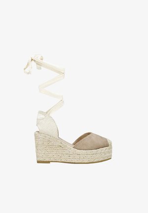 Alpargata beige con cuña, puntera cerrada, suela trenzada de yute y largas cintas crema para atar alrededor del tobillo.