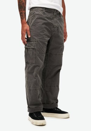 Grå cargo bukser lavet af et bomuldsblend, med store sidelommer, afslappet pasform og synlige syninger. Sammen med sorte sneakers.