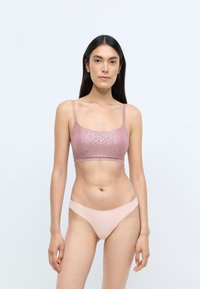 Lyserød blonde bralette med tynde stropper og glatte, sømløse lyserøde trusser. Bralletten har et fint blomstermønster og en tætsiddende silhuet.