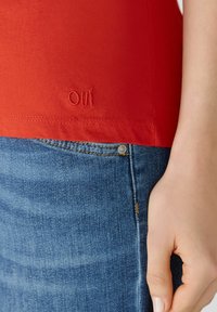 Rode katoenen tanktop met de tekst "OUI" geborduurd aan de zoom, gecombineerd met blauwe denim jeans met een metalen knoop en een subtiele wassing.