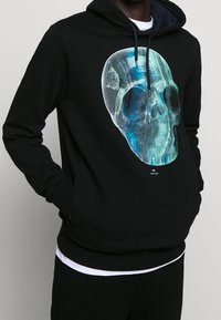 Černá mikina s kapucí s velkým průhledným motivem lebky v odstínech modré a zelené. Obsahuje kapuci se stahovací šňůrkou a klokánovou kapsu.
