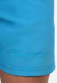 Pantaloni corti azzurri realizzati in tessuto liscio, con un logo ricamato discreto di un blu più scuro vicino all'orlo. Fit regolare e design essenziale.