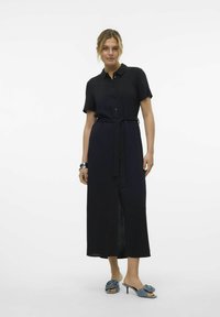 Robe chemise noire à manches courtes, avec un devant boutonné, une taille ceinturée et une fente sur le côté. Assortie à des mules à talons bleues avec un détail floral.