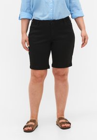 Pantalones cortos negros con una textura suave, de longitud hasta la rodilla con dobladillo enrollado. Combinados con sandalias marrones y una camisa de botones azul clara.