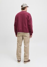 Sudadera burdeos con cuello redondo y corte relajado, combinada con chinos beige y zapatillas marrones. Tela suave, diseño minimalista.