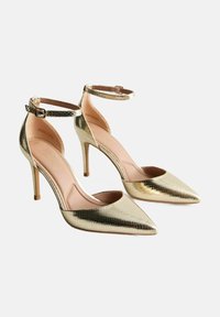 Zapatos de tacón alto dorados con punta afilada, superficie texturizada y correa en el tobillo con detalle de hebilla. Plantilla y tacón de color rosa suave.