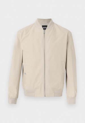 Jachetă bomber bej deschis cu fermoar frontal, buzunare laterale cu capse, guler, manșete și tiv striate. Țesătură moale și netedă.