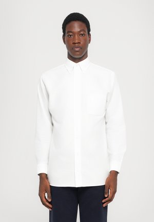 Camisa blanca de botones, hecha de algodón, con cuello, mangas largas y un bolsillo en el pecho del lado izquierdo. Textura suave.