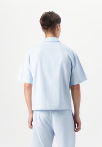 Light blue short-sleeve shirt made of textured fabric, featuring a straight hem and a classic collar. Paired with matching shorts.