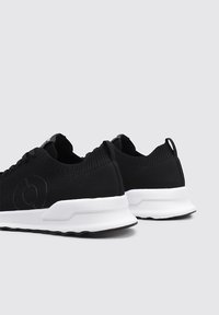 Zapatillas deportivas negras con parte superior de tejido texturizado, entresuela blanca y suela de goma. Presenta una lengüeta de tiro y un discreto detalle del logo en el lateral.