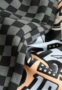 Material pătrat în negru și gri, combinat cu un material cu model ce prezintă culori moi precum piersica și albastru deschis cu desene grafice.