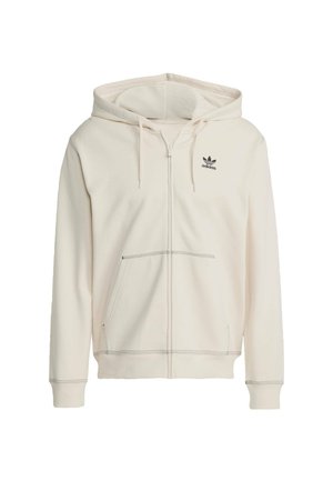 Krémová zipovací mikina vyrobená z měkké tkaniny, s kapsou typu klokanka, nastavitelnou kapucí na šňůrku a černým logem Adidas na hrudi.