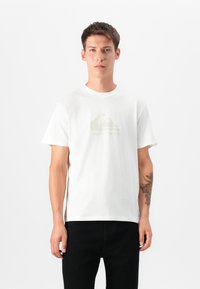 T-shirt de algodão branco com gola redonda e mangas curtas, apresentando um discreto design de logótipo cinza no peito. Ajuste simples e clássico.