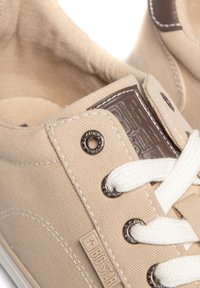 Beežid kanvasnike valged paelad, ümmargused hõbedased silmadega ja tumepruun nahkdetail keelel, millel on mullitud bränding.