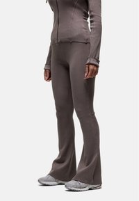 Veste zippée marron à côtes associée à un pantalon flare ajusté assorti, tous deux en tissu doux et extensible. Des chaussures de sport grises viennent compléter le look.