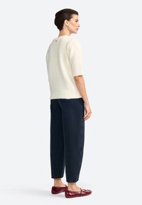 Pull en tricot crème à manches courtes, associé à un pantalon large bleu marine et des ballerines bordeaux ; présente un ourlet côtelé et un détail de boutons au dos.