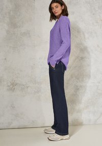 Pull en tricot violet avec une coupe décontractée, des manches longues et une texture côtelée. Associé à un jean bleu foncé et des chaussures de sport de couleur claire.