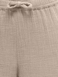 Gros plan sur un pantalon beige en tissu texturé avec une taille élastique et un cordon noué à l'avant au centre.
