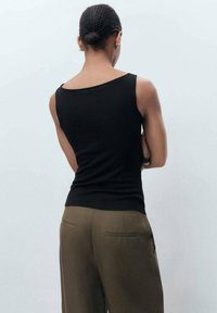 Zwarte, strakke tanktop met een bootcut halslijn, gecombineerd met olivegroene wijde broekspijpen. Zachte textuur, minimalistisch ontwerp, geen zichtbare patronen.