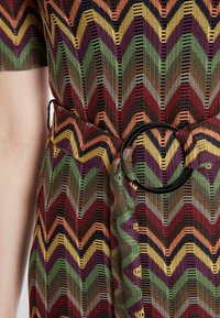 Multifarbene Kleid mit Zickzackmuster in Rot-, Grün-, Orange- und Gelbtönen. Enthält einen breiten schwarzen runden Gürtel und strukturierten Stoff.