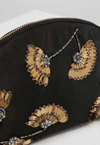 Zwarte stoffen zakje met gouden pailletbloemmotieven en zilveren kralenaccenten, afgewerkt met een gouden ritssluiting.