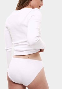 Witte geribbelde lange mouwtop gecombineerd met witte onderkleding. De top heeft een ronde halslijn en aansluitende mouwen. Gladde textuur, minimalistisch ontwerp.