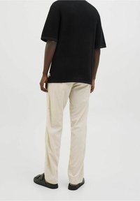 Černá texturovaná košile s krátkým rukávem, béžové lehké kalhoty a černé sandály. Košile má kulatý výstřih a nenápadnou značku s logem.